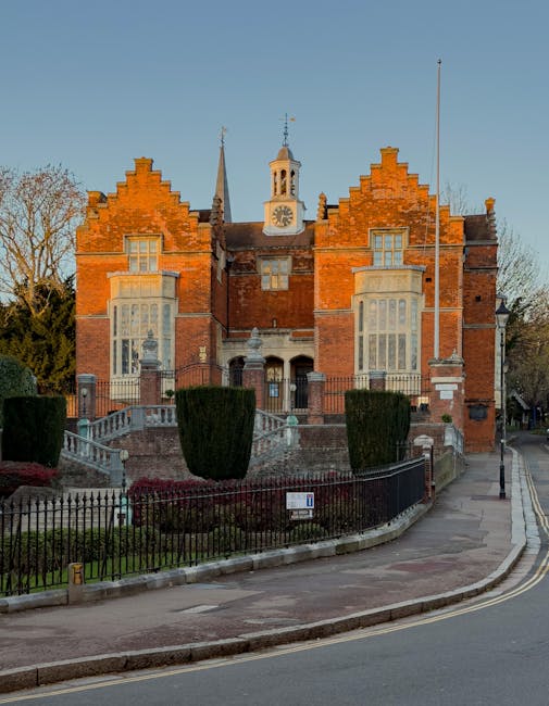 A two-storey residential house with a brick facade on the right side and a white-painted wall on the left side, situated behind a paved street. The building features white-framed sash windows on both